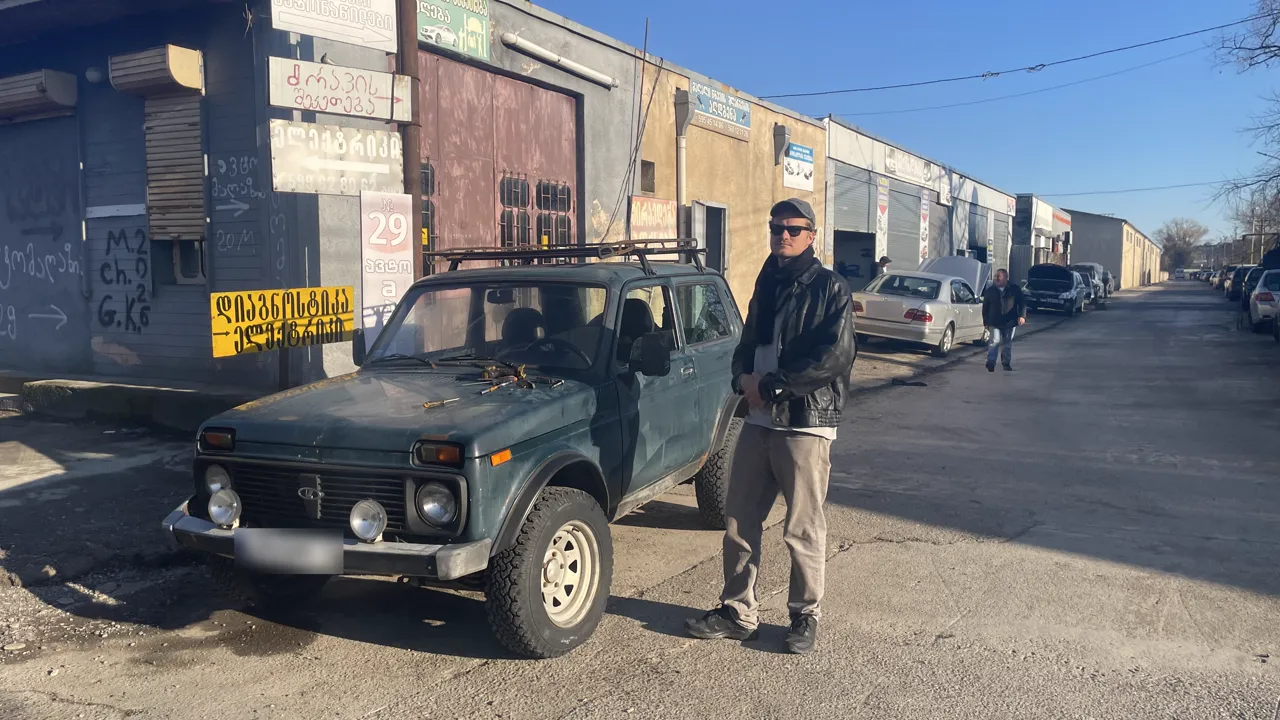 Alex in Georgia, next to an old Lada in a street of car workshops